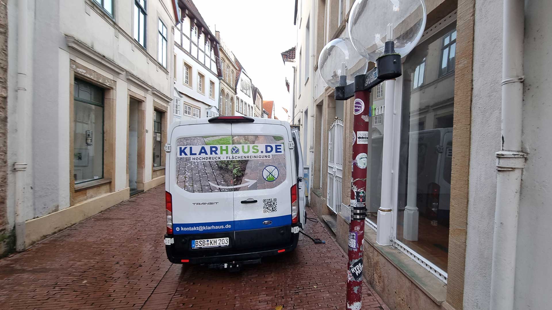 Transporter in enger Gasse, Aufschrift KLARHUS.DE, weiße Karosserie, gepflasterte Straße.