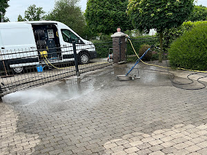 Eine Person bedient ein Hochdruckreinigungsgerät auf einer gepflasterten Auffahrt.