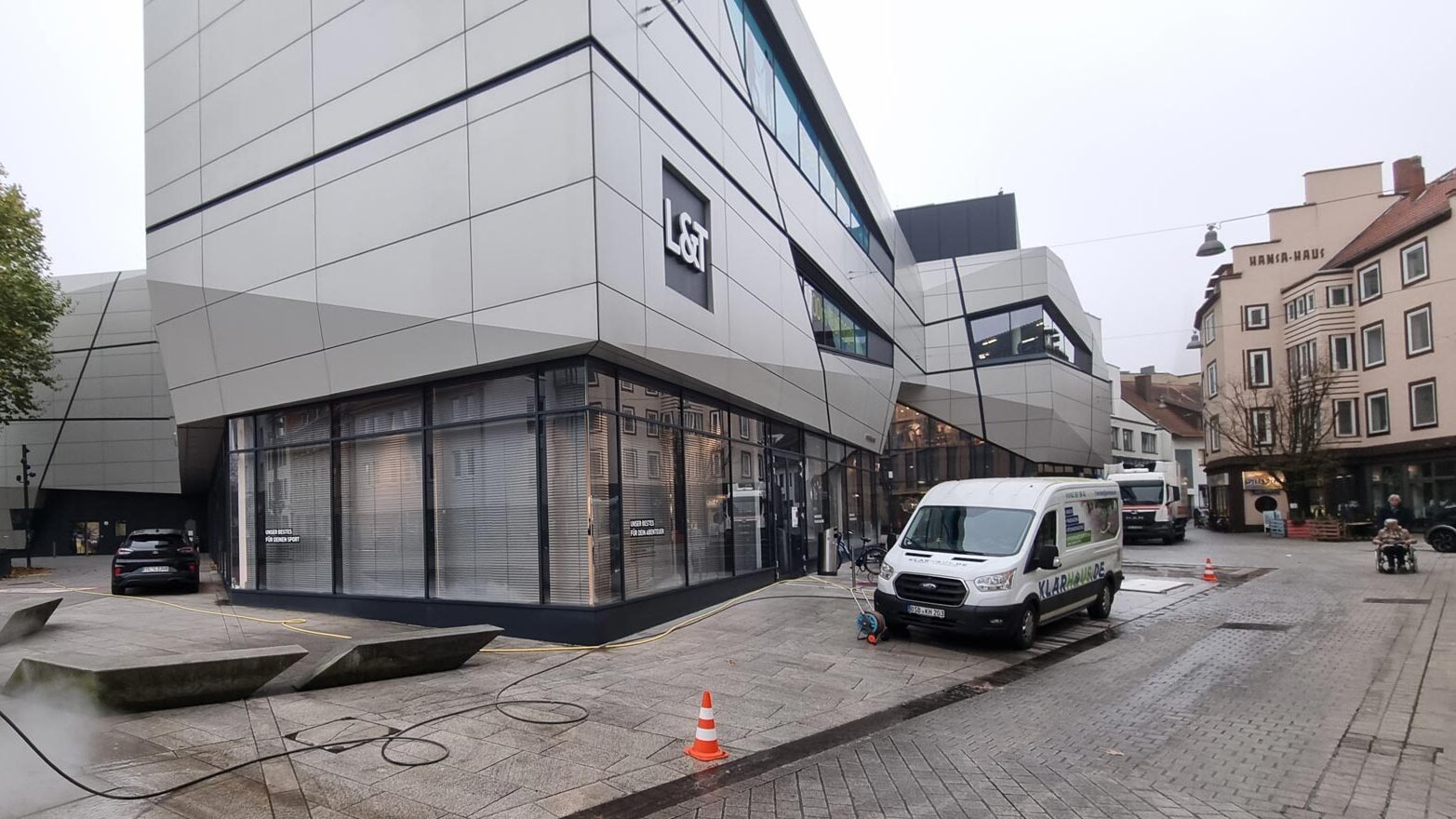 Außenansicht eines Geschäftsgebäudes, Arbeiter reinigt Fliesen mit Hochdruckreiniger.