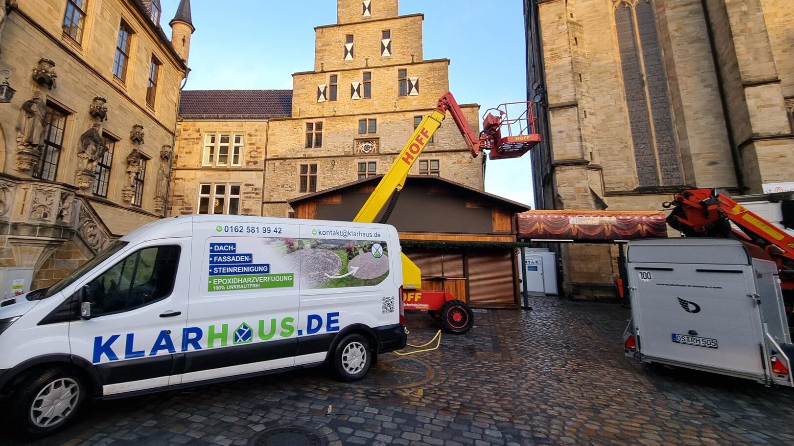 Transporter und Bauarbeiter neben einer Hebebühne vor einem historischen Gebäude und Turm.
