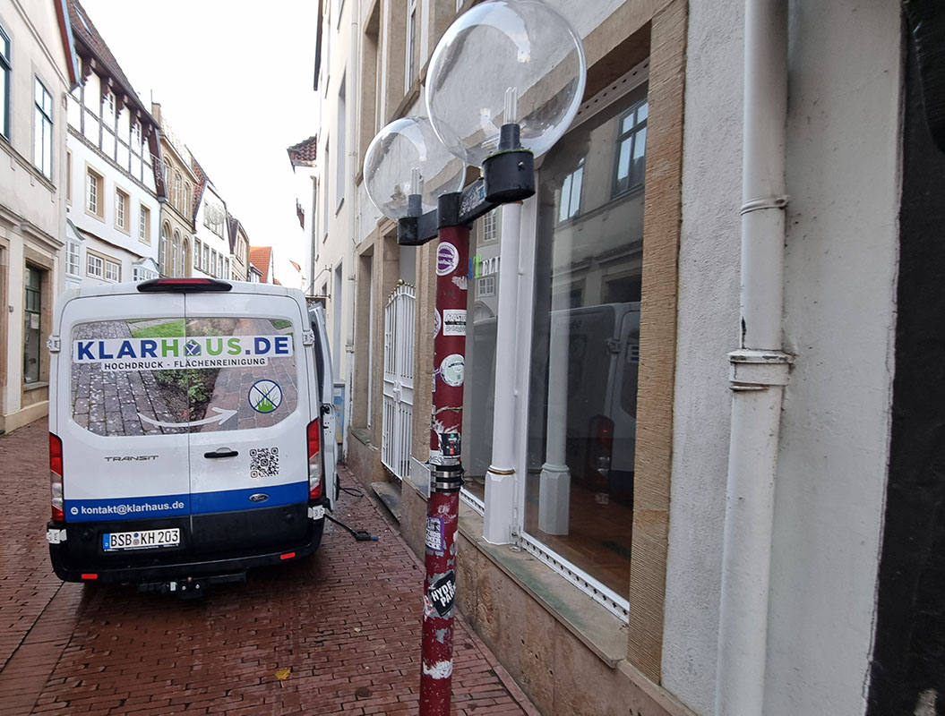 Ein weißer Lieferwagen mit blaugrüner Werbung steht in einer engen Altstadtgasse