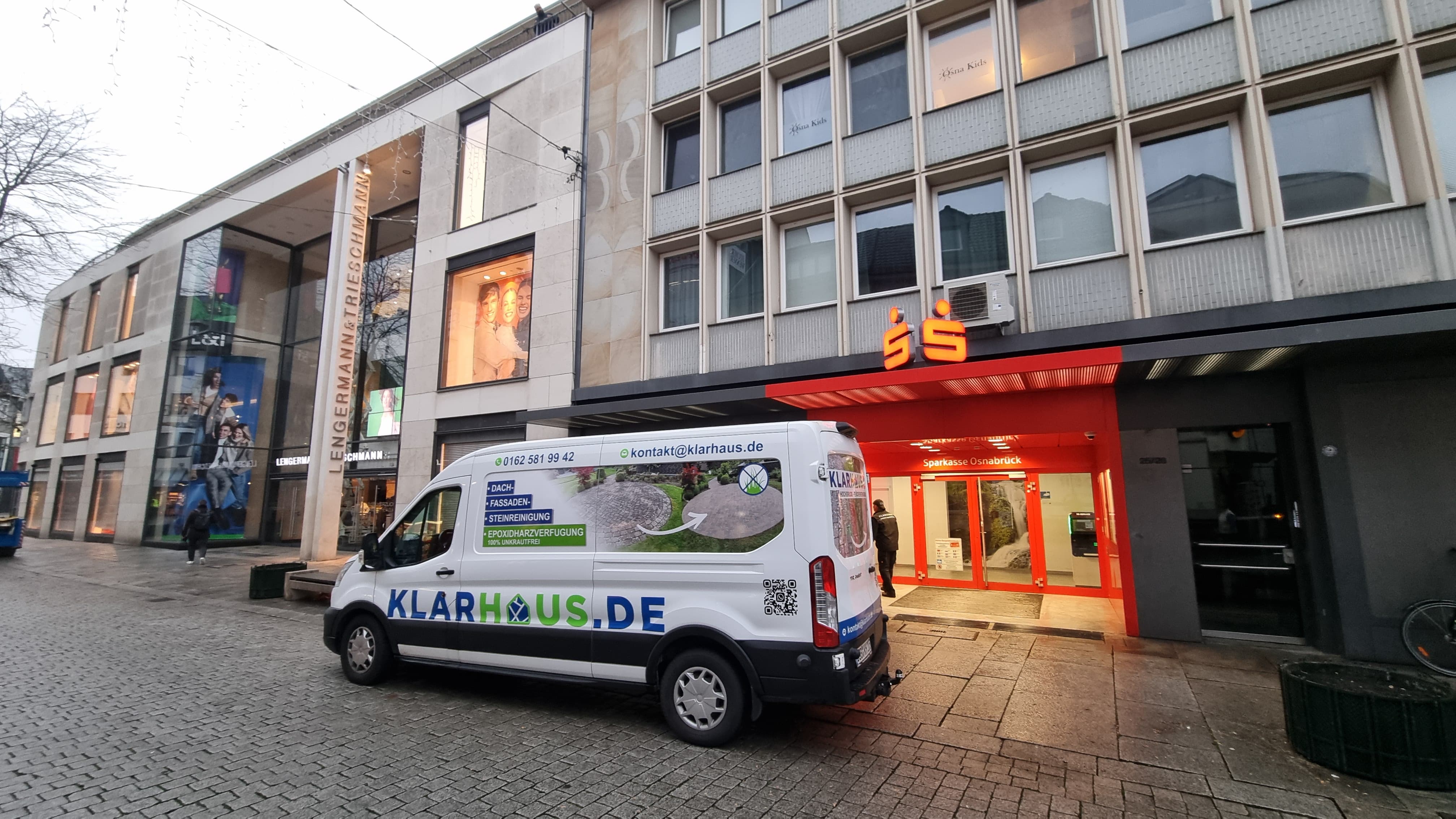 Ein weißer Lieferwagen von KLARHAUS mit grün-blauer Beschriftung steht vor einem modernen Gebäude mit orangefarbenem Eingang und Glasfassade