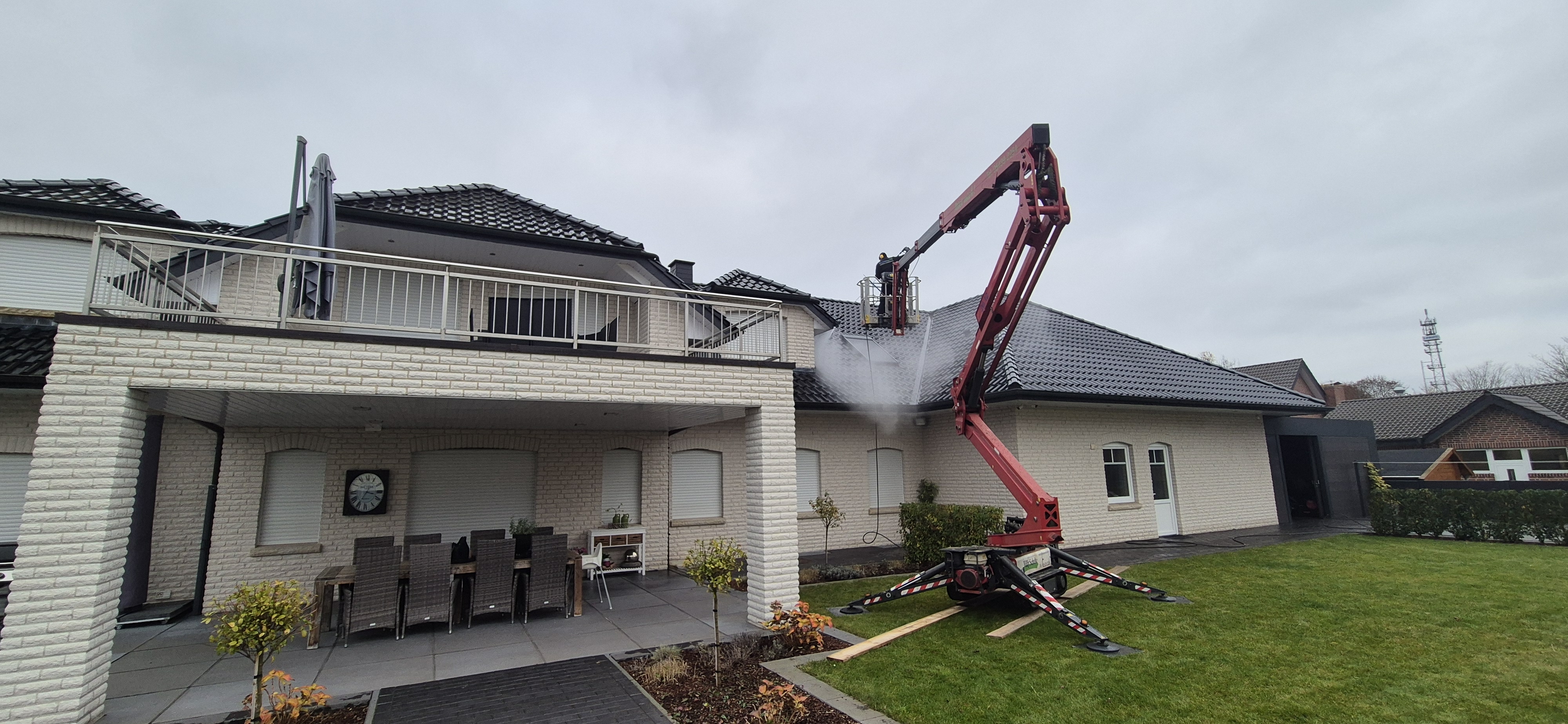 Ein roter Kran mit Greifarm arbeitet an einem hellen Haus mit schwarzem Dach