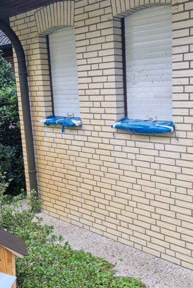 Zwei hochgeschobene weiße Rollläden mit blauen Paketen auf den Fensterbänken