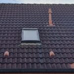 Ein braunes Ziegeldach mit kleinem Fenster, silbernem Schornstein und Licht im Hintergrund