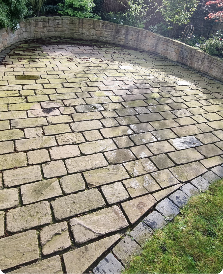 Ein sonniger, von Moos überzogener Steinplatz mit Randmauer und nassem Boden
