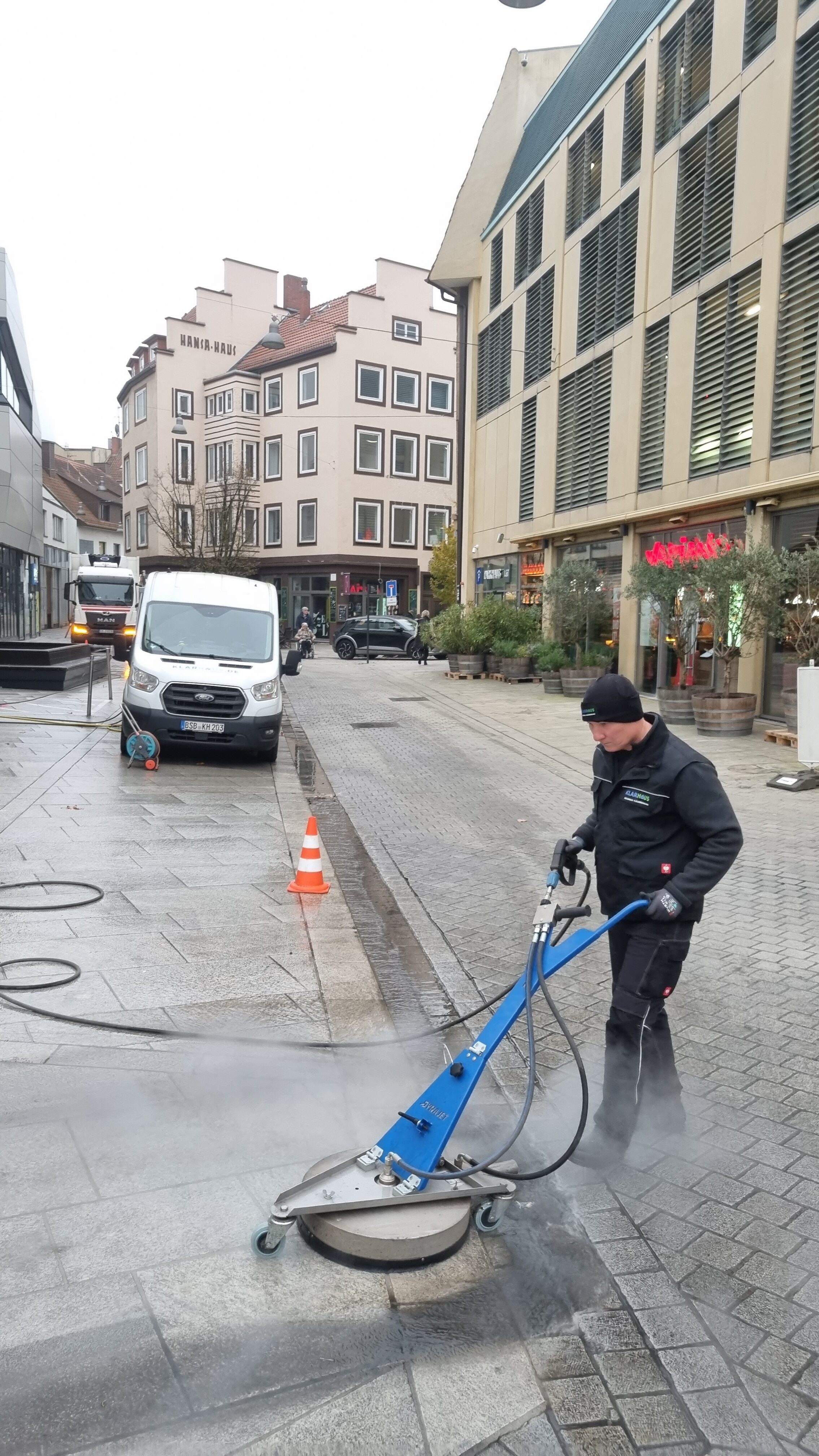 Ein Mann mit konzentriertem Blick reinigt grau gepflasterte Straßen mit einer Maschine