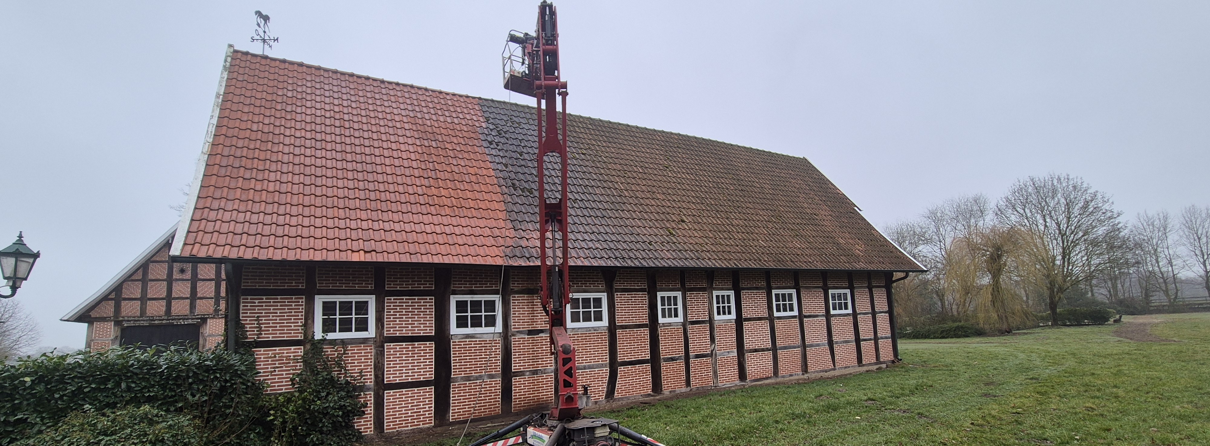 Ein rotes Hebebühnenfahrzeug steht vor einer Fachwerkscheune mit gereinigtem Dachbereich