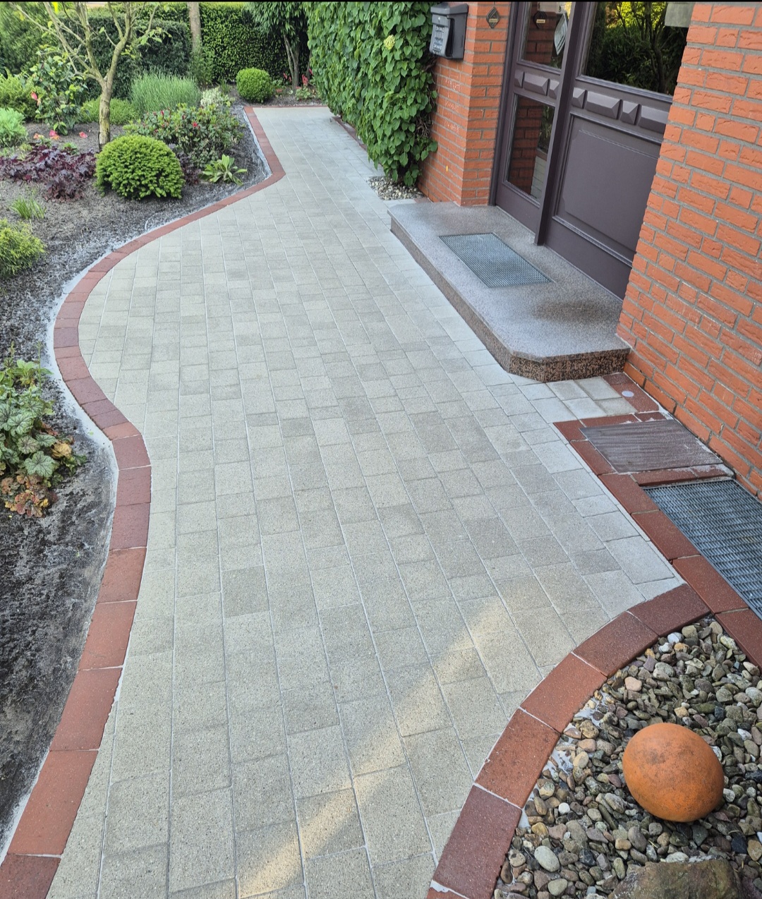 Gepflasterter Weg mit roten und grauen Steinen führt geschwungen zum Hauseingang