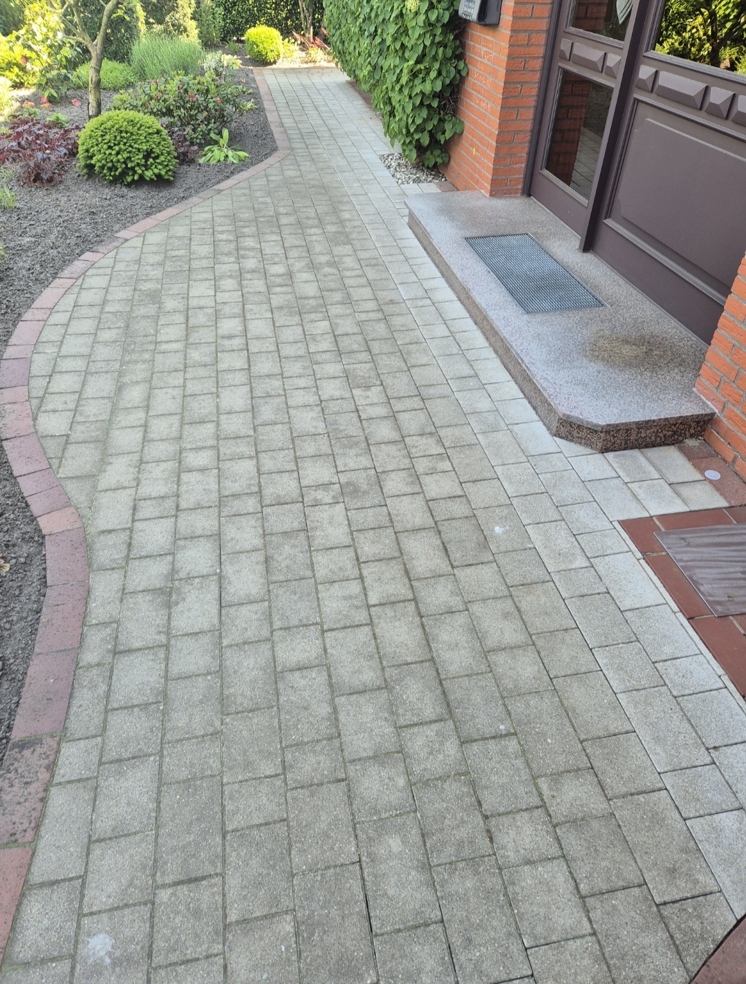 Gepflegter gepflasterter Weg führt zu einer Haustür mit Backstein und Pflanzen