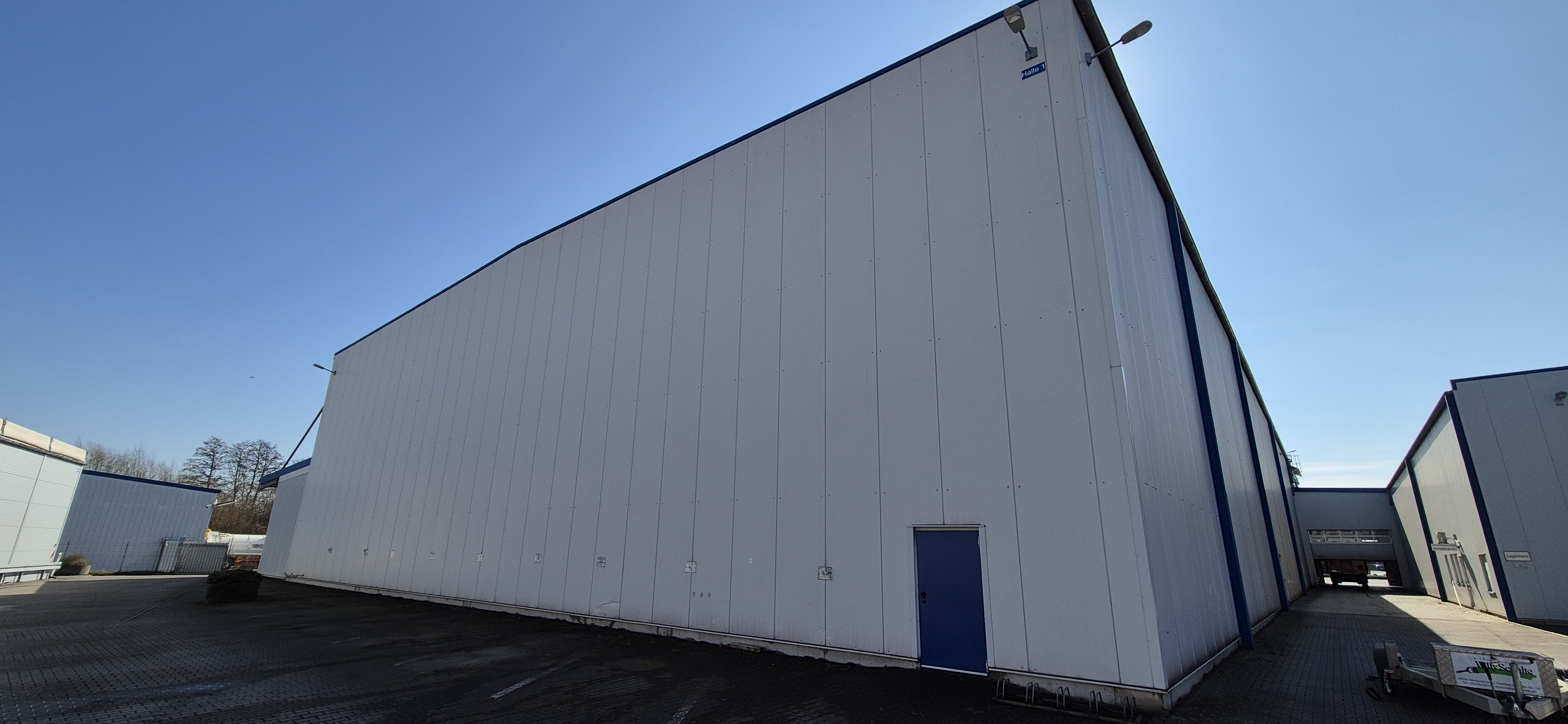 Ein großes weißes Industriegebäude mit blauer Tür bei sonnigem Wetter