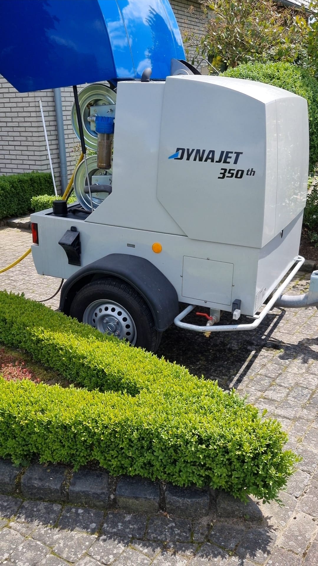 Mobiler Hochdruckreiniger DynaJet 350th in Grau mit blauer Abdeckung auf Gehweg