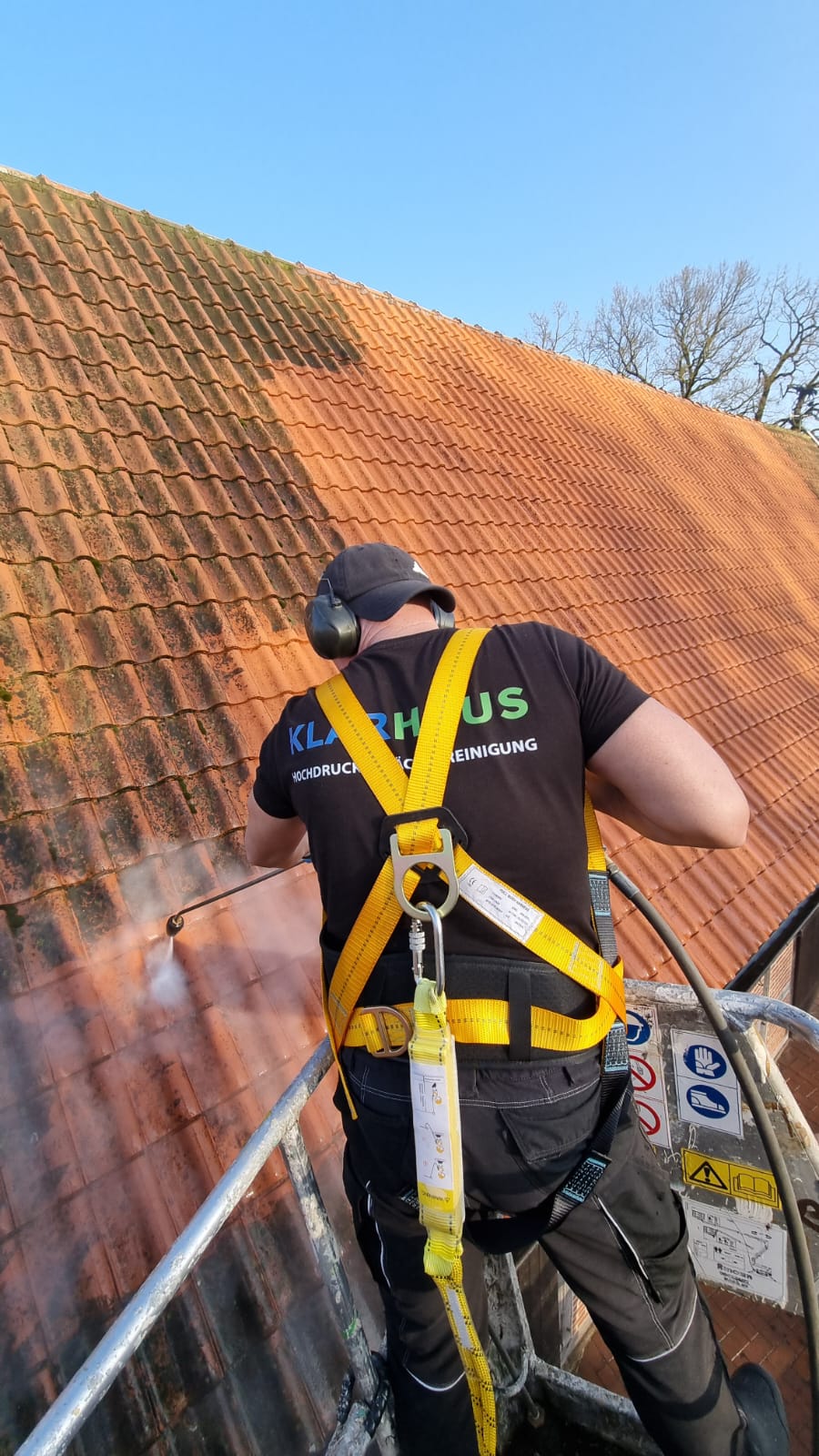 Ein Mann mit schwarzem TShirt und Sicherheitsgurt reinigt ein rotbraunes Dach