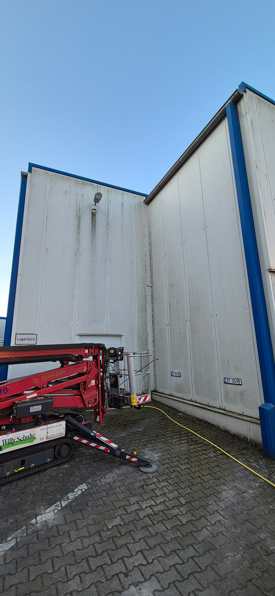 Eine große weiße Industriehalle mit roten Hubarbeitsbühnen und gelben Kabeln davor