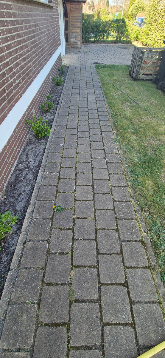 Ein langer grauer gepflasterter Weg verläuft entlang eines Hauses mit Backsteinwand