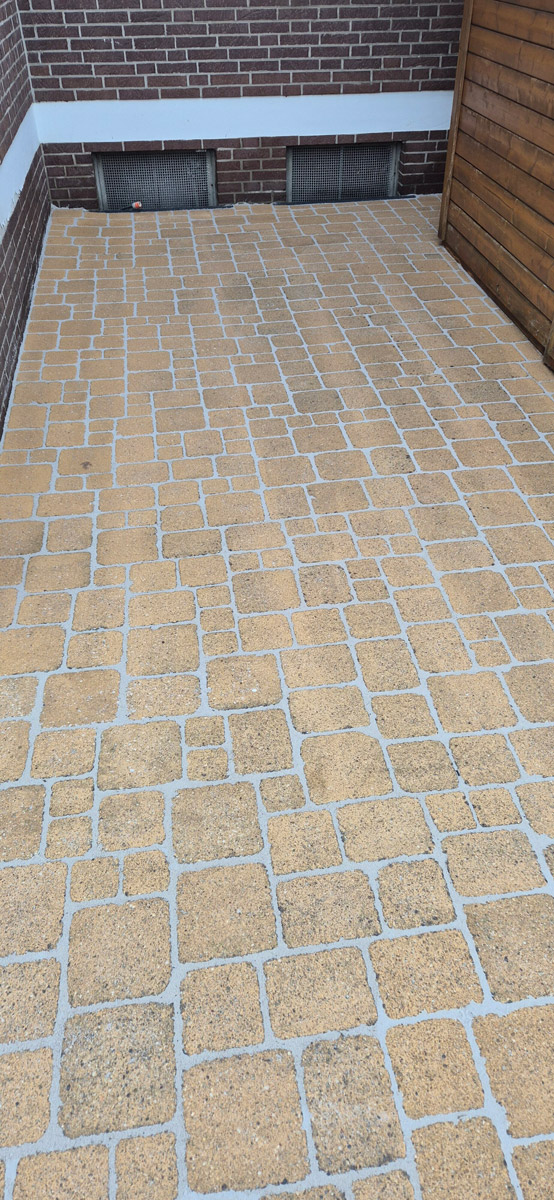 Gelber gepflasterter Hof mit rechteckigen Steinen vor brauner Ziegelwand