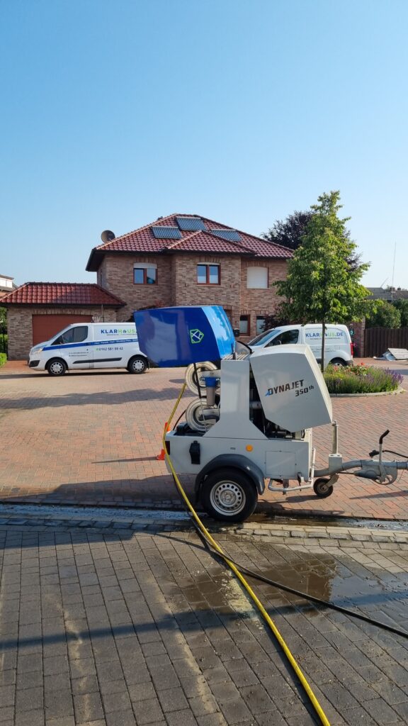 Eine Maschine mit blauem Schutzdeckel steht auf einem gepflasterten Hof vor Wohnhäusern
