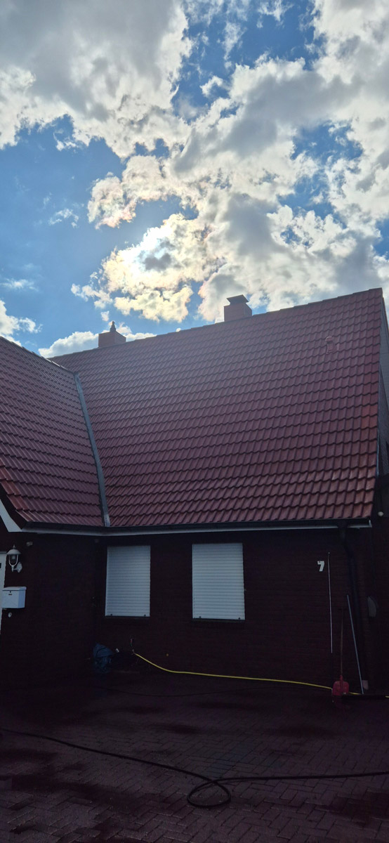 Rotes Ziegeldach unter dramatischem Himmel mit Wolken und Sonnenstrahlen