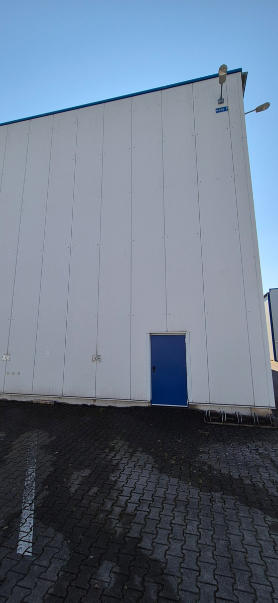 Weiße Gebäudewand mit kleiner blauer Tür und Überwachungskamera bei klarem Himmel