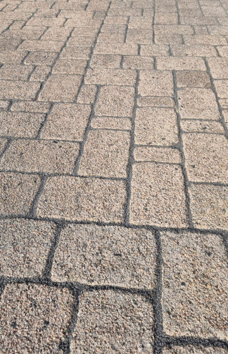 Heller gepflasterter Gehweg mit sandfarbenen Steinen und unregelmäßigen Linien