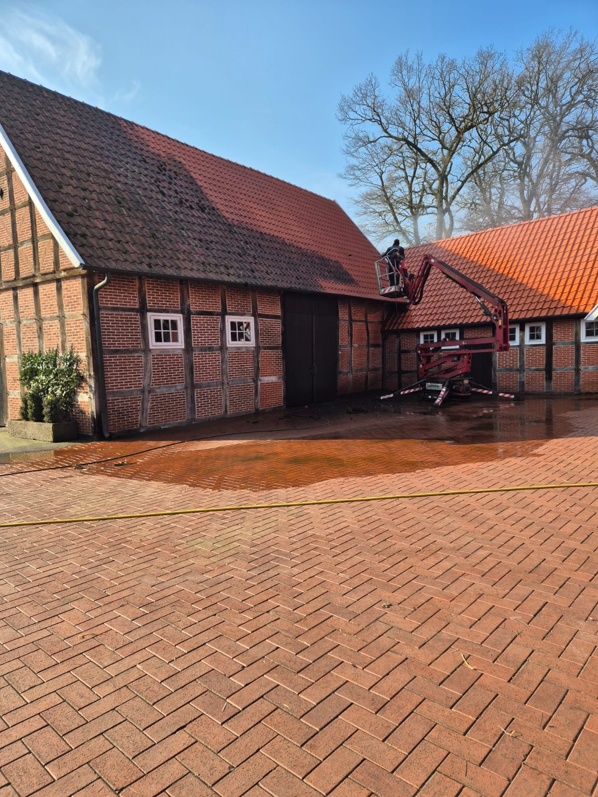 Eine Person reinigt mit einer Hebebühne das rote Ziegeldach eines Bauernhauses